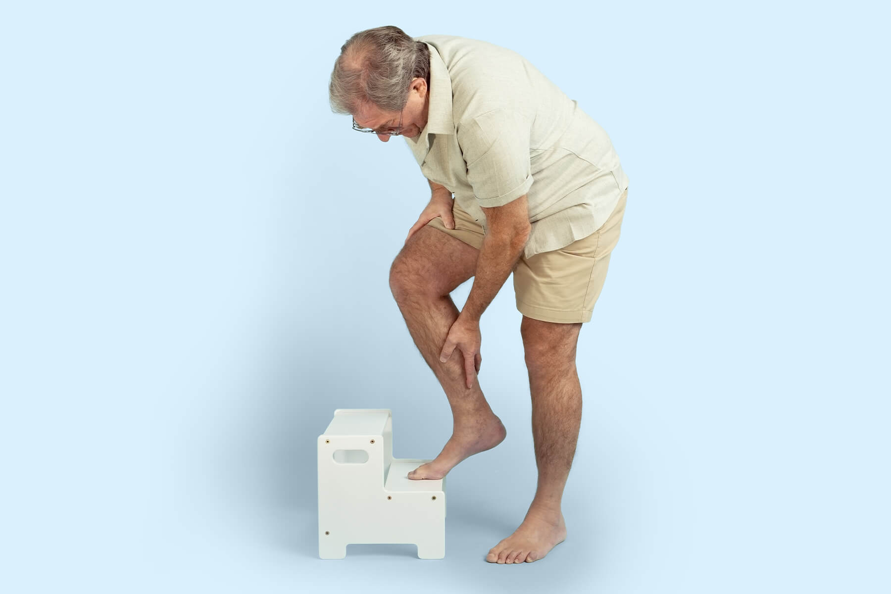 Man holding his aching calf with one foot resting on a step stool