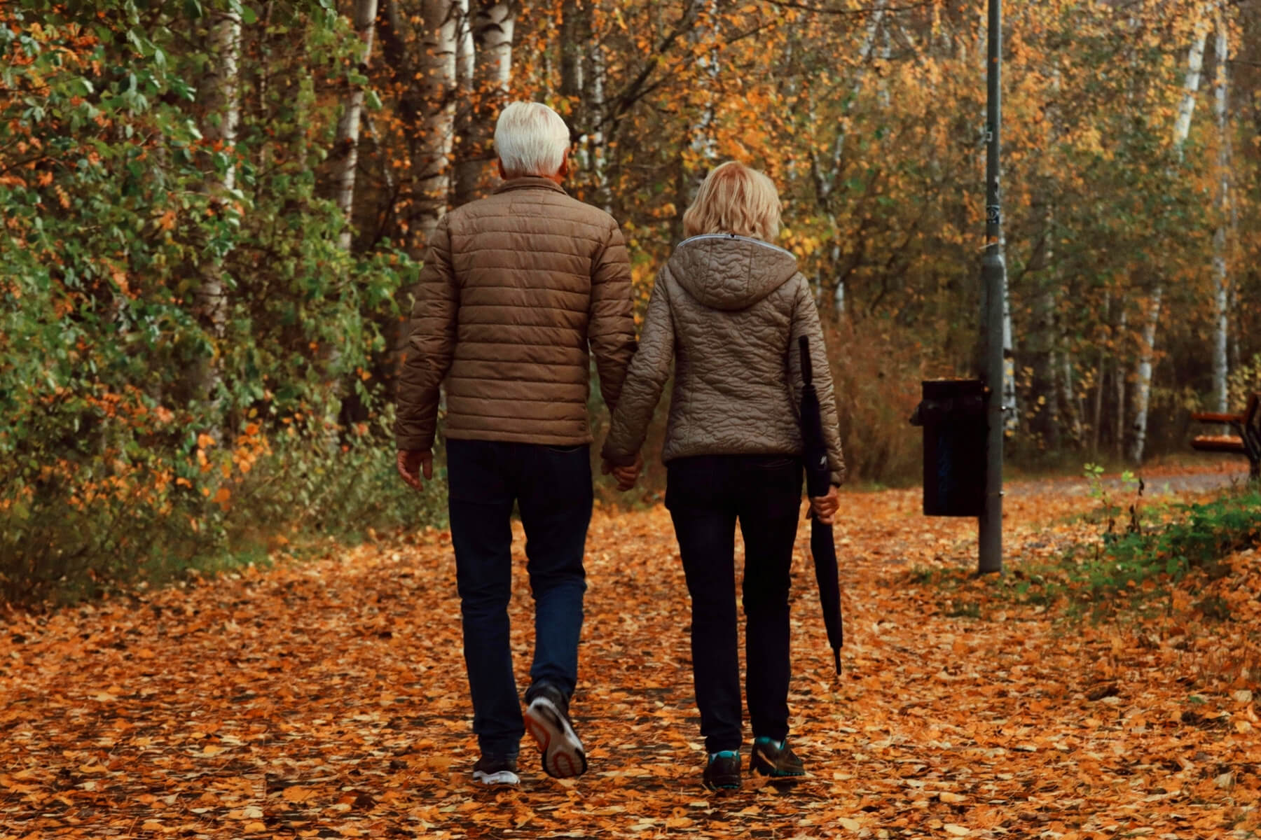 Pareja caminando por un sendero cubierto de hojas en un parque en otoño